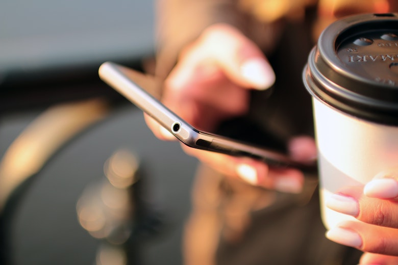 A person with a phone and coffee in-hand